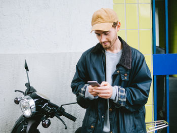 Young man using mobile phone while standing against wall