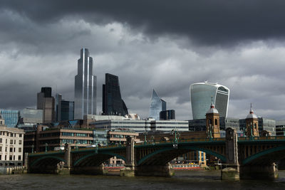 Bridge over river by buildings against sky in city