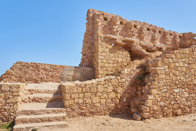 An old brick wall with stairs and clear blue sky in the background.