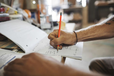 Cropped image of carpenter writing on document at table in workshop