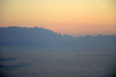 Scenic view of silhouette mountains by boats in sea against orange sky during sunrise