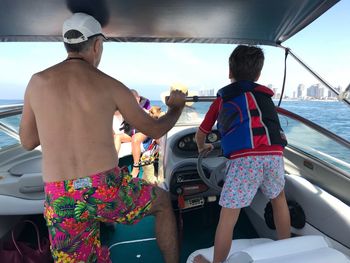Rear view of shirtless man with son driving boat in sea