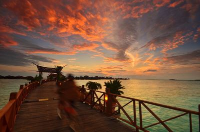 Blurred motion of person riding bicycle on pier over sea against sky during sunrise