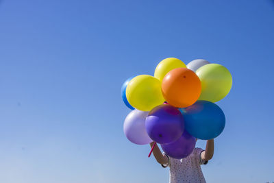Low angle view of boy holding multi colored balloons against clear blue sky