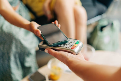 Close up view at hand hold mobile phone, touch a credit card reader inside the coffee shop. 