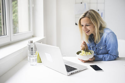 Businesswoman talking on laptop during video call while eating food at home