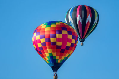 Low angle view of 2 hot air balloons floating in a clear blue sky on a sunny day