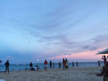 People enjoying on beach against sky during sunset