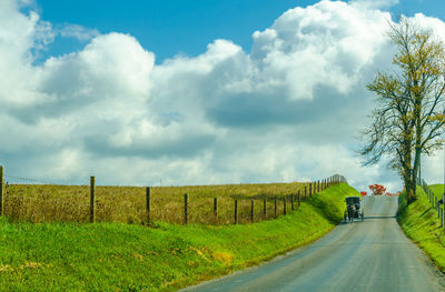 Country road amidst field against sky