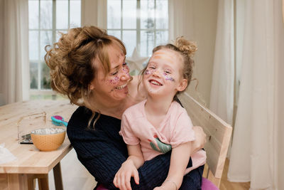 Mother and daughter laughing playing dress up with make up at home