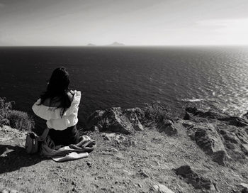 Woman sitting on rock looking at sea