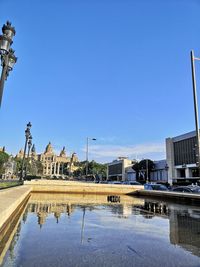 Reflection of buildings in lake against clear blue sky