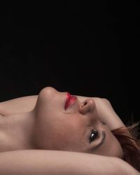 Close-up portrait of woman lying down against black background