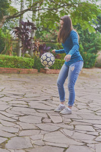 Young woman playing with soccer ball on footpath at park