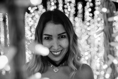 Portrait of woman standing by illuminated lights at night