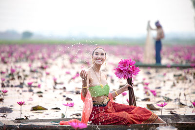 Smiling young woman holding water lilies in boat on lake