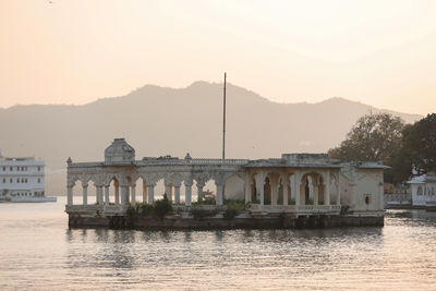 Buildings by river against sky during sunset