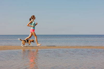 Full length of woman jumping at beach against clear sky