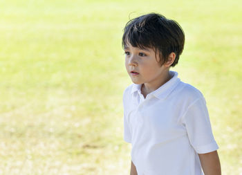Boy looking away while standing on field