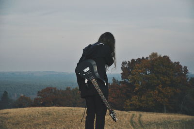 Rear view of man standing on field with guitar