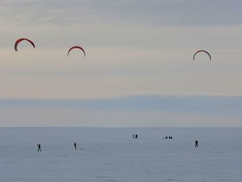 People in sea against sky during sunset