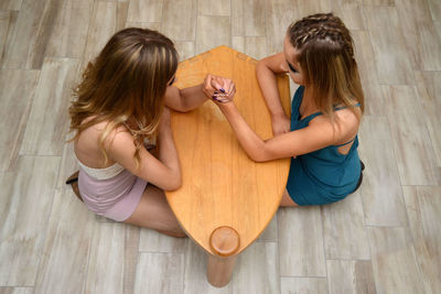 High angle view of sisters arm wrestling at wooden table on floor