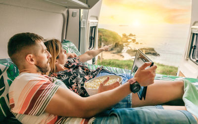 Couple watching a movie on the tablet eating popcorn lying on the bed of their camper van