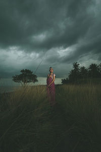 Young woman standing on grassy field against cloudy sky
