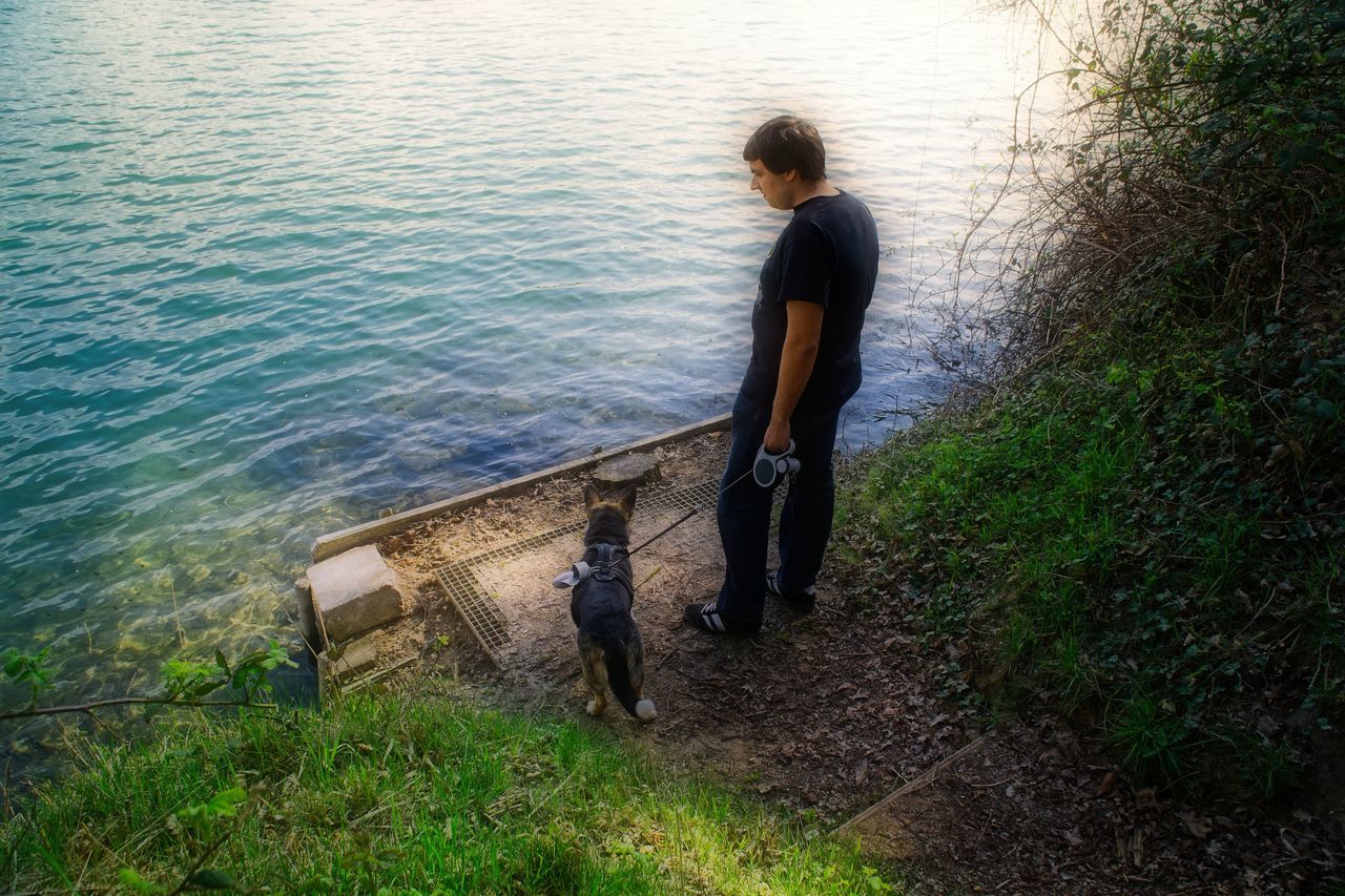 water, full length, plant, nature, grass, casual clothing, one person, men, one animal, day, high angle view, real people, mammal, lifestyles, fishing, leisure activity, outdoors, pet owner