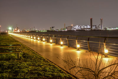 Illuminated factory by river against sky at night