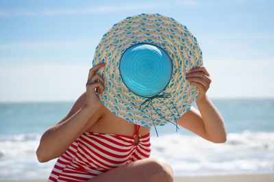 Midsection of woman wearing hat on beach against sky