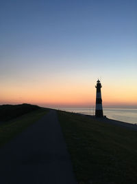 Lighthouse by building against sky during sunset