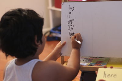 Rear view of boy writing on whiteboard at home