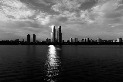 Sea by modern buildings against sky in city