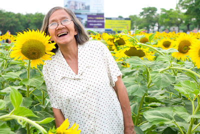 Midsection of woman with sunflower standing against yellow flowering plants