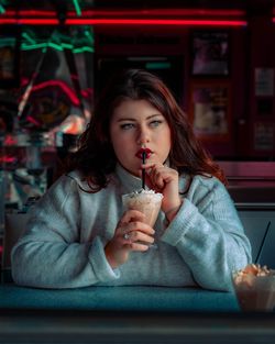 Thoughtful woman having drink while sitting at table in restaurant