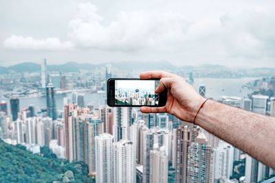 Midsection of man using mobile phone against buildings in city