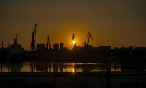 Silhouette buildings by river against sky during sunset