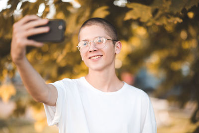 Happy smiling teen boy 15-17 year old making selfie photo with smart phone over green nature 