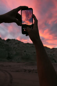 Man photographing smart phone against sky during sunset