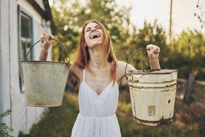 Smiling woman holding buckets while standing outdoors