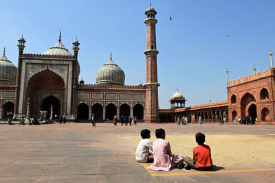 Rear view of boys sitting outside jama masjid in city