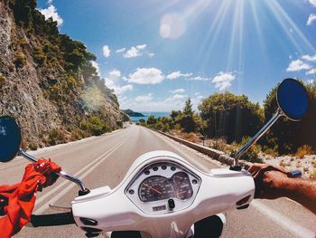 Cropped image of man riding motor scooter on road during sunny day