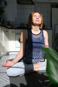 Portrait of young woman sitting in lotus yoga position at home