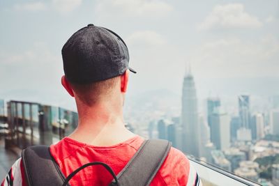 Rear view of young man with backpack against cloudy sky in city