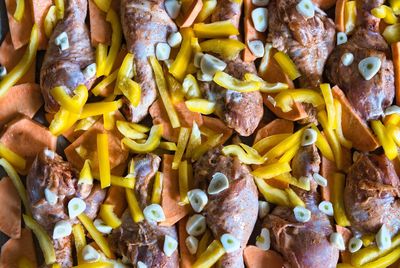 Chicken legs with sweet potato, yellow pepper and garlic before roasting in the oven. top view.