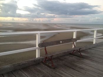 Empty benches on beach against sky