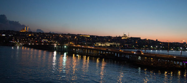 Illuminated buildings by river against sky at night