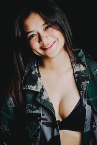 Portrait of smiling young woman against black background