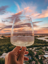Close-up of hand holding wine glass against sky
